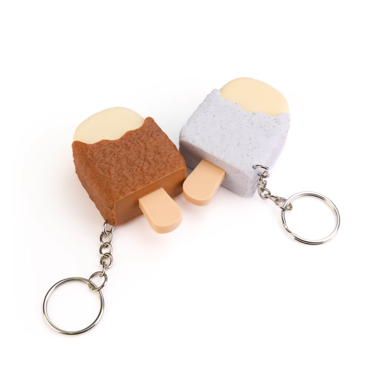 Two small novelty keychains shaped like ice cream popsicles, one brown and one light gray, shown on a plain white background.