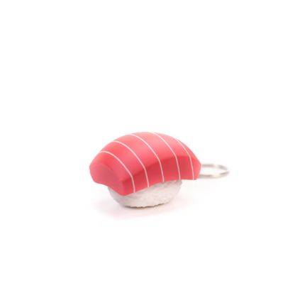 A small sushi-shaped accessory, likely a charm or keychain, featuring a pink and white striped top resembling tuna or salmon nigiri with a white base, shown on a plain white background.