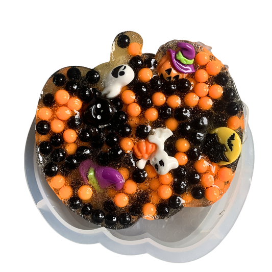 Close up of pumpkin shaped picky pad filled with black and orange beads and halloween ghost charms.